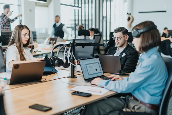 Professionals working at laptops with audio headsets in a collaborative office environment.