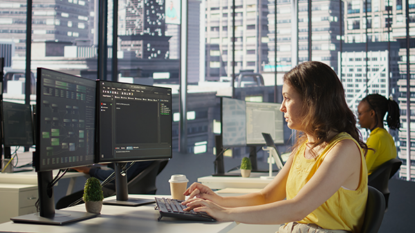 Professional working on multiple computer screens displaying data in a modern office.