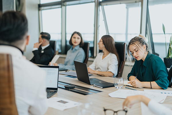 Professionals working around a table with laptops and notes during a meeting.