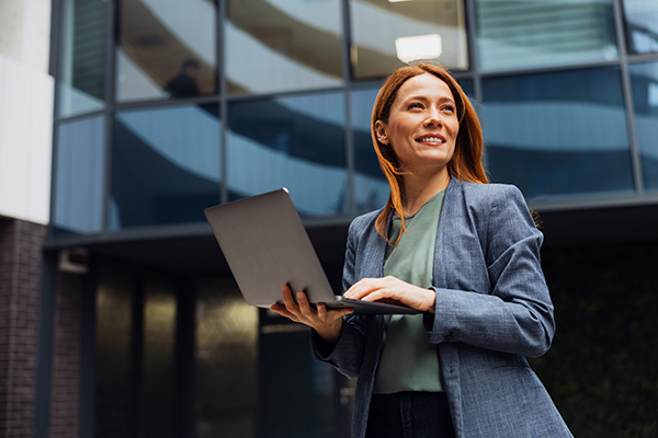 Professional holding a laptop while standing outside a modern office building