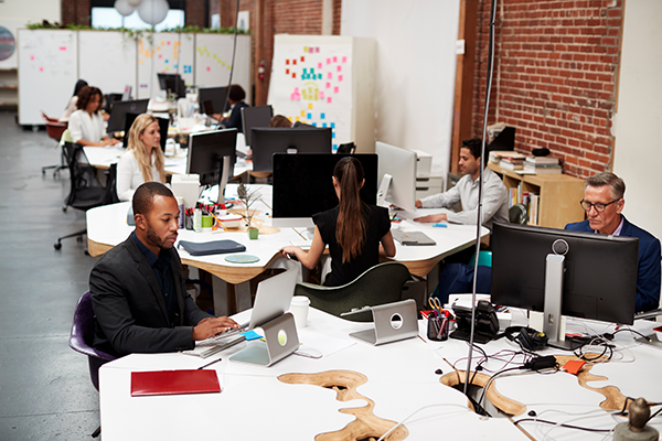 Professionals working on laptops at desks in a modern open-plan office environment.