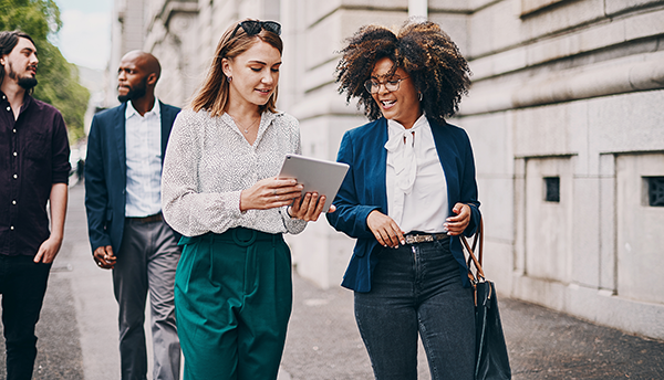 Professionals walking outdoors while reviewing a tablet in an urban setting.