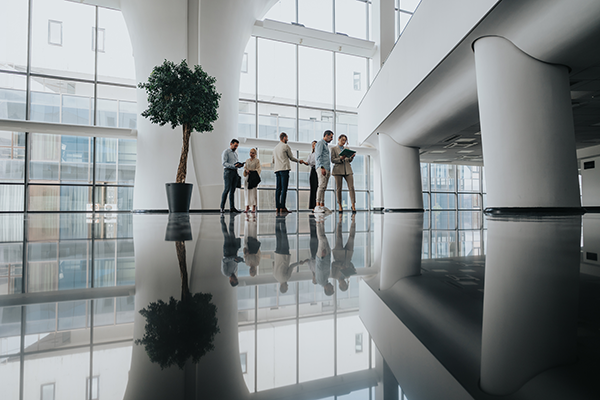 Group of professionals standing and discussing in a large modern office atrium with glass walls.