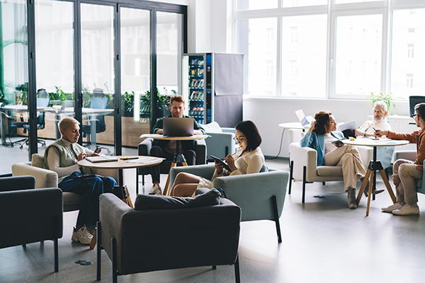 Professionals working independently on laptops and mobile devices in a modern shared office lounge.