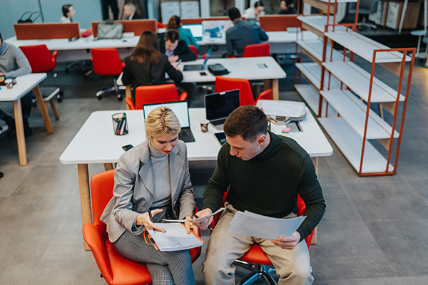 Professionals reviewing documents together while seated in an open-plan office environment.