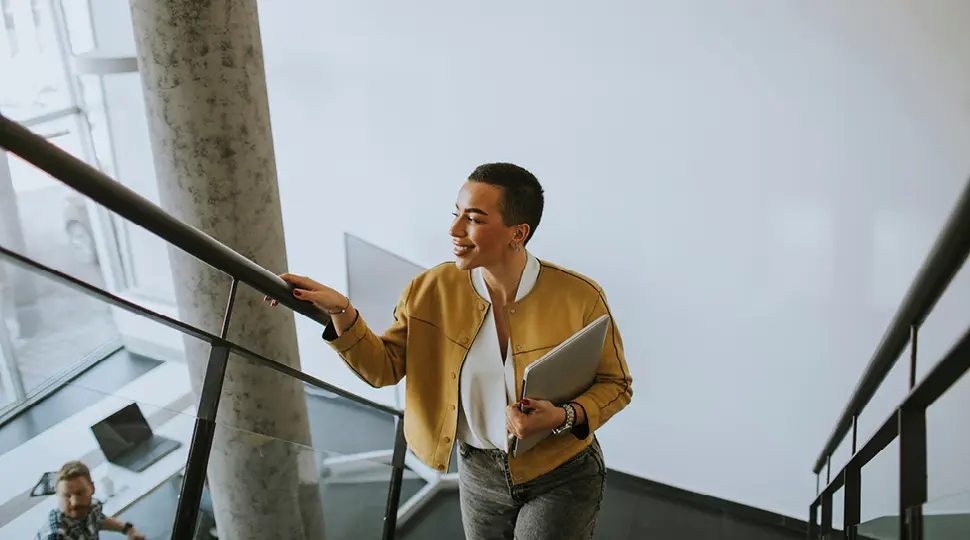 Person walking up a staircase while carrying a laptop.