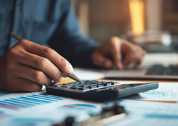 Close-up of a person using a calculator while reviewing financial reports.