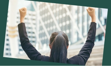 Person raising both arms outdoors in front of office buildings.