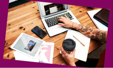 Person working on a laptop at a desk with a tablet and coffee cup.