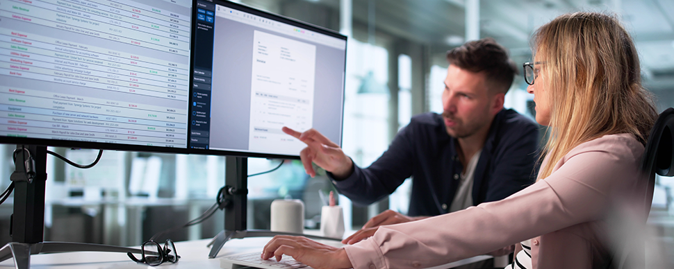 Professionals reviewing data on dual computer monitors.