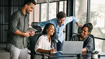 Group of professionals gathered around a laptop collaborating in a modern office setting