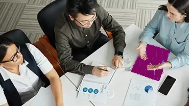 Overhead view of professionals reviewing printed charts and financial data while discussing around a white desk.