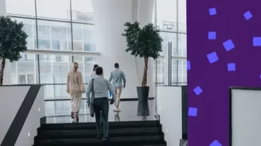 Professionals walking up stairs in a modern office atrium with large windows.