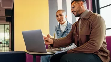 Two professionals using a laptop together in a modern office.