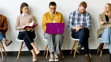 Professionals seated in a row reviewing documents and devices in a waiting area.