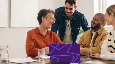 Professionals collaborating around a laptop during a meeting in a modern office.