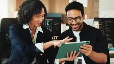 Two professionals reviewing content on a tablet in an office.