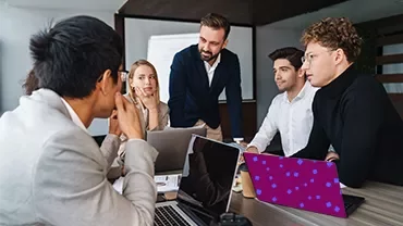 Professionals in a meeting around laptops in a modern office.