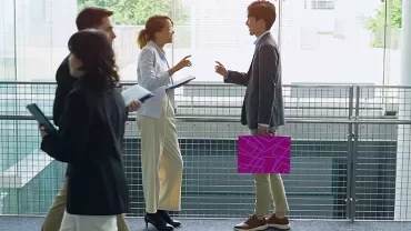 Business professionals walking and talking in a modern office building corridor.
