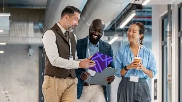 Three colleagues walking through an office corridor while reviewing information on a tablet.