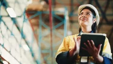 Person wearing a hard hat and holding a tablet inside an industrial facility.