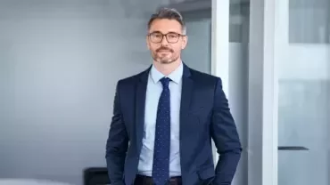 Professional standing in a modern office wearing a business suit.