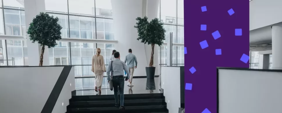 Professionals walking up stairs in a modern office atrium with large windows.
