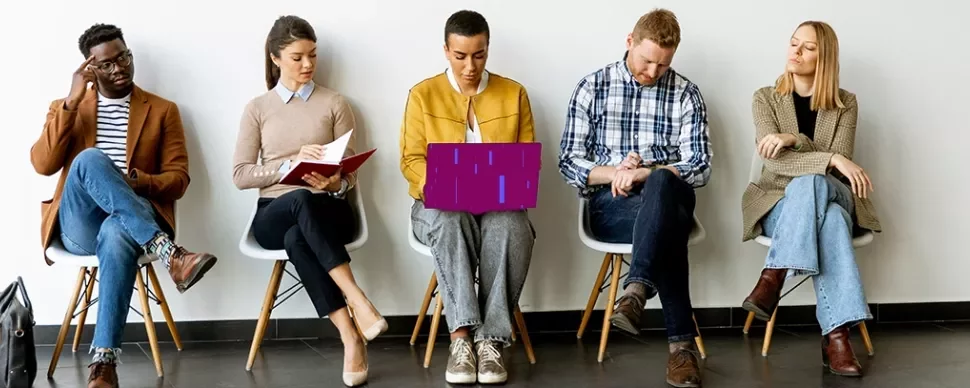 Professionals seated in a row reviewing documents and devices in a waiting area.