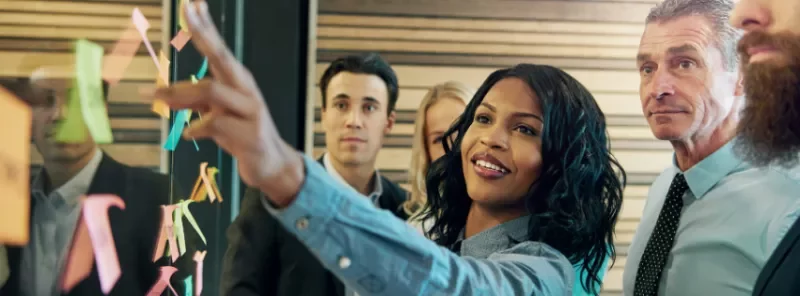 a woman pointing to a post it next to a group of people