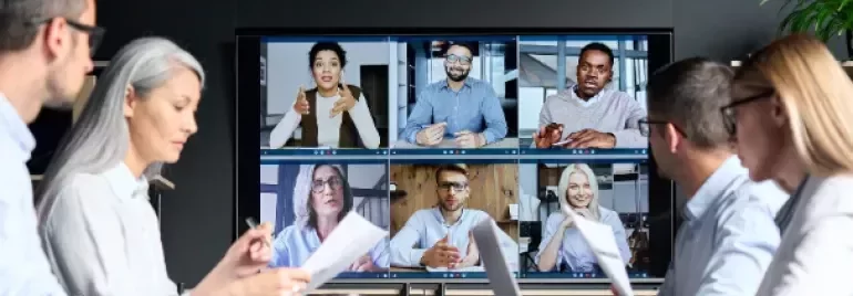 Professionals participating in a hybrid meeting with colleagues joining via video conference on a large screen.