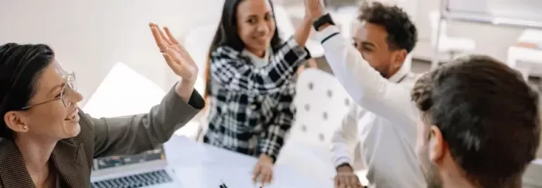 Professionals collaborating during a meeting and celebrating success with a high-five.