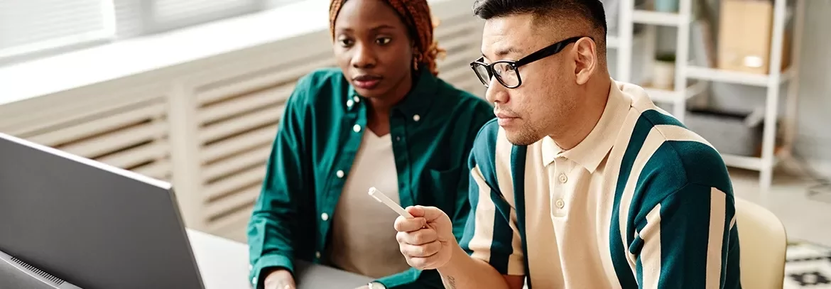 Two professionals reviewing information on a desktop monitor in an office.