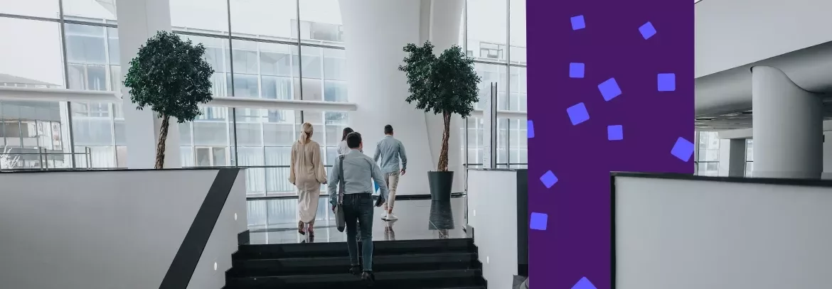Professionals walking up stairs in a modern office atrium with large windows.