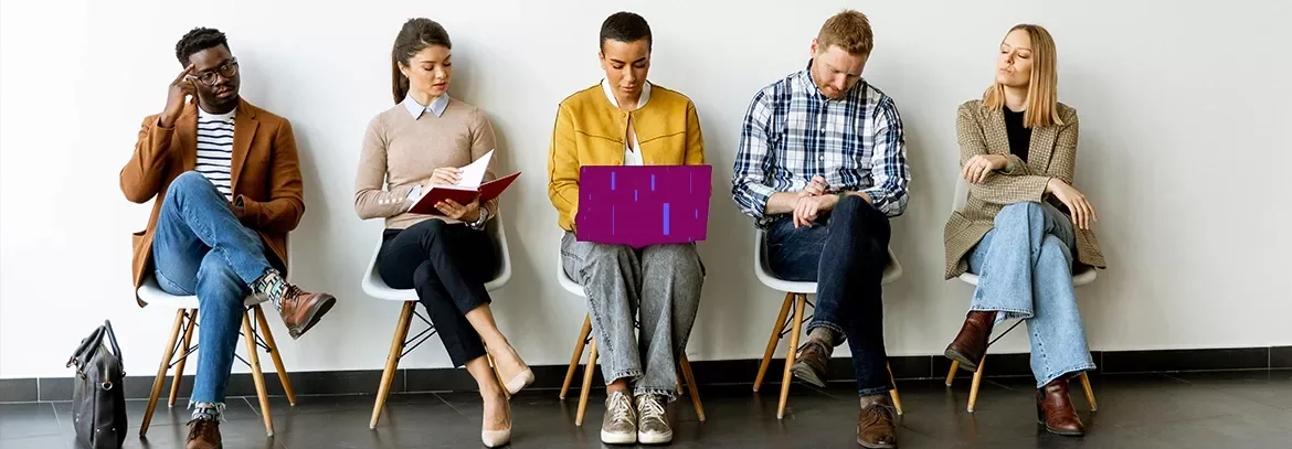 Professionals seated in a row reviewing documents and devices in a waiting area.