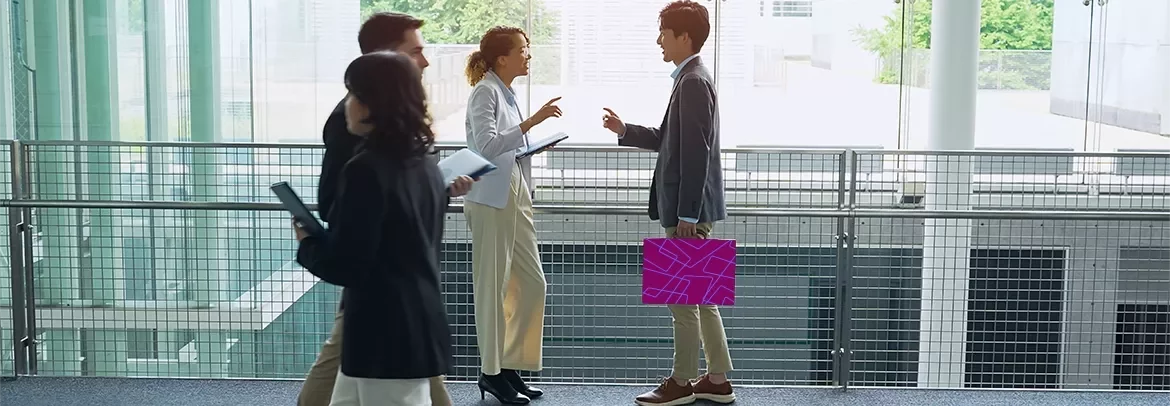 Business professionals walking and talking in a modern office building corridor.