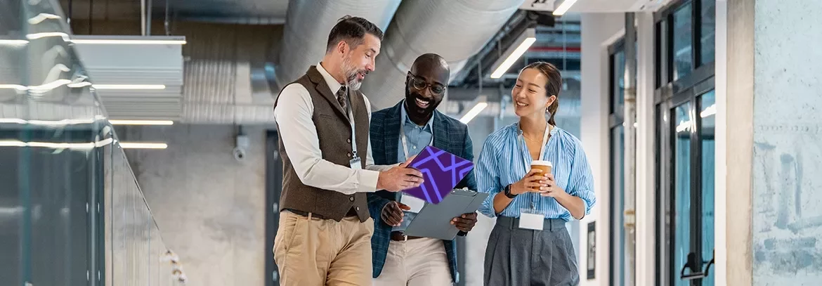 Three colleagues walking through an office corridor while reviewing information on a tablet.