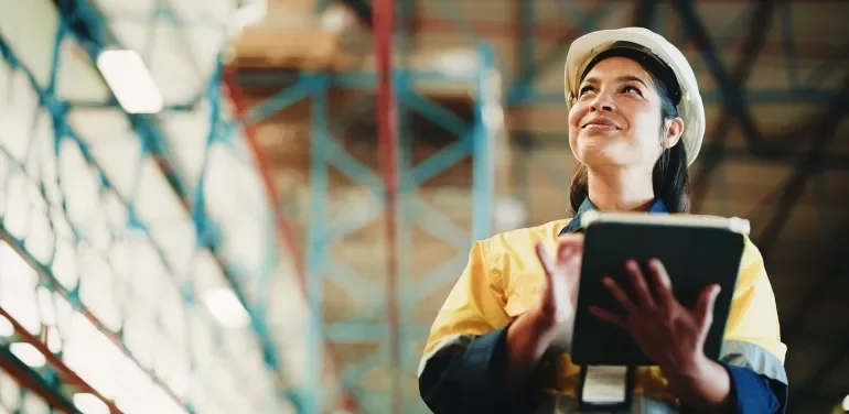 Person wearing a hard hat and holding a tablet inside an industrial facility.