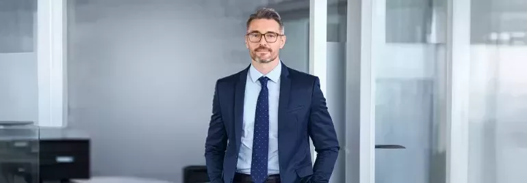 Professional standing in a modern office wearing a business suit.