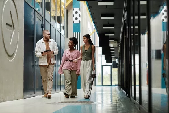 Three colleagues walking and talking through a modern office hallway.